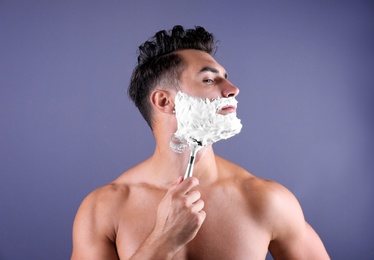 Handsome young man shaving on color background