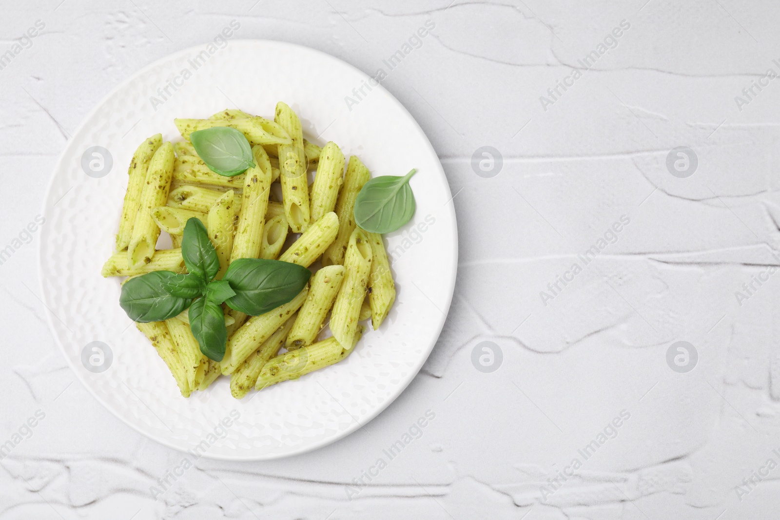 Photo of Delicious pasta with pesto sauce and basil on white textured table, top view. Space for text