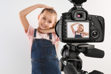 Photo of Cute little blogger recording video against white background, focus on camera