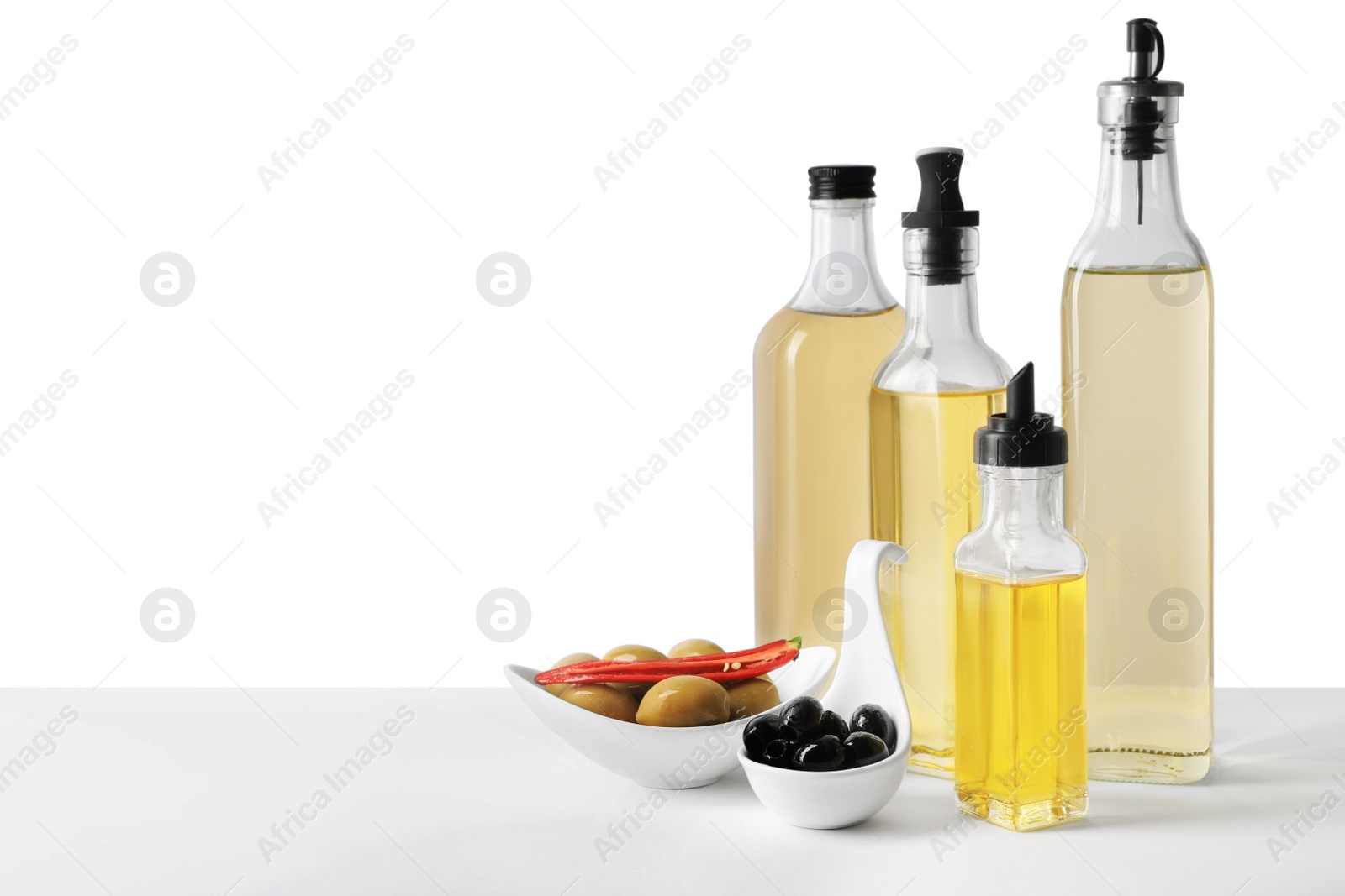 Photo of Bottles of different cooking oils and olives on white background