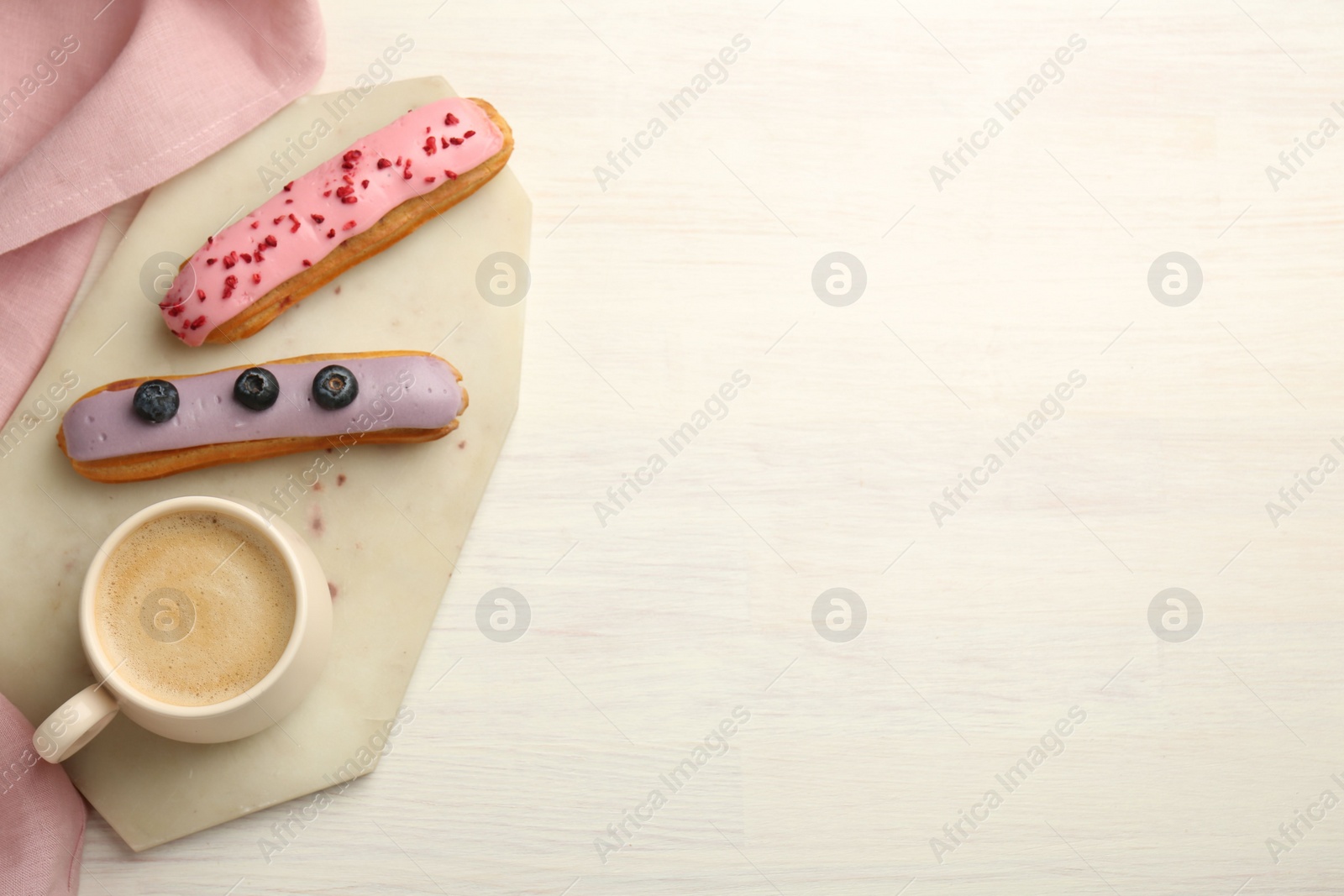 Photo of Cup of coffee and delicious eclairs covered with glaze on white wooden table, top view. Space for text