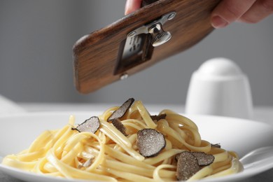 Photo of Woman slicing truffle onto fettuccine at table, closeup