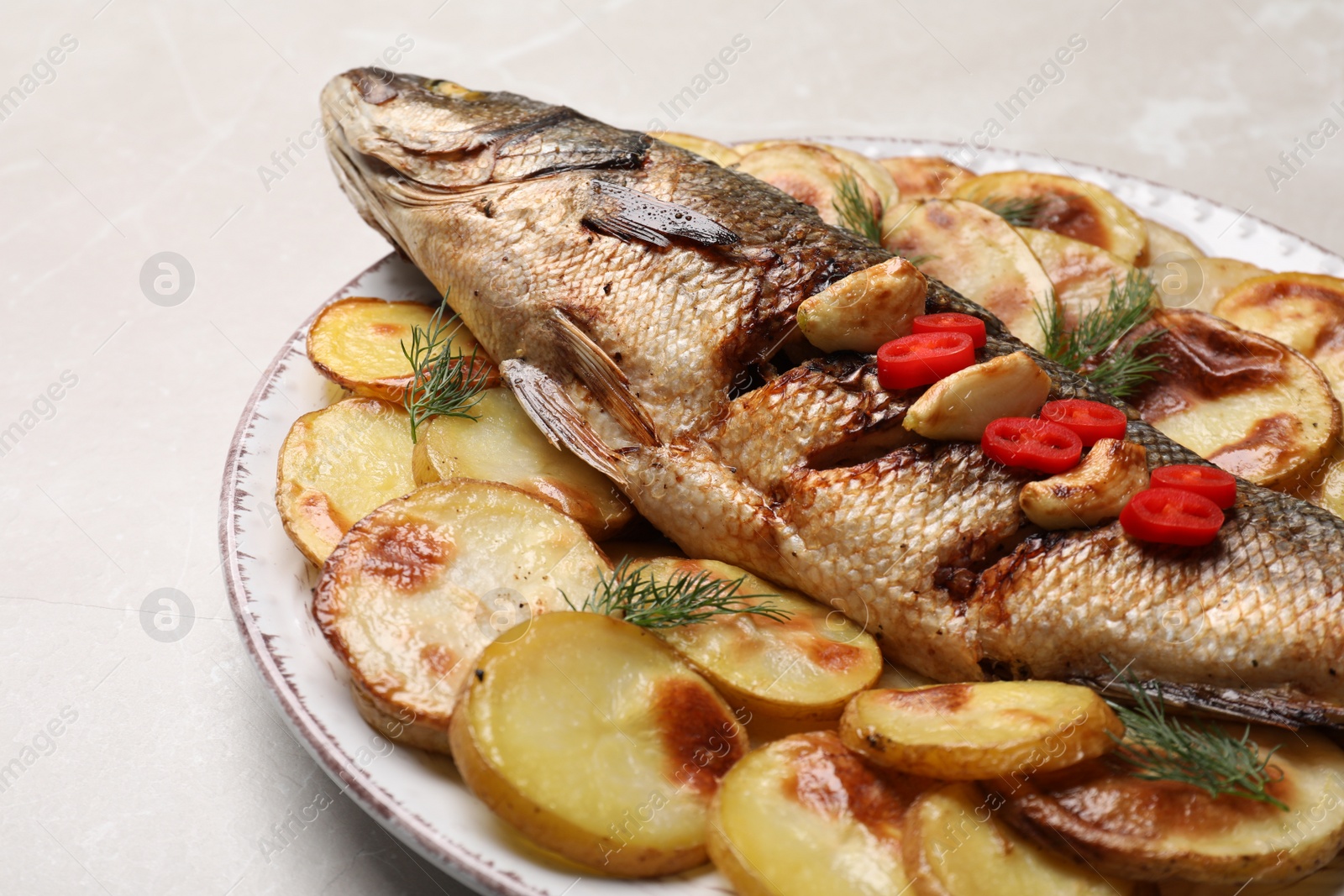 Photo of Plate with delicious baked sea bass fish and potatoes on light table, closeup