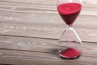 Photo of Hourglass with pink flowing sand on wooden table. Space for text