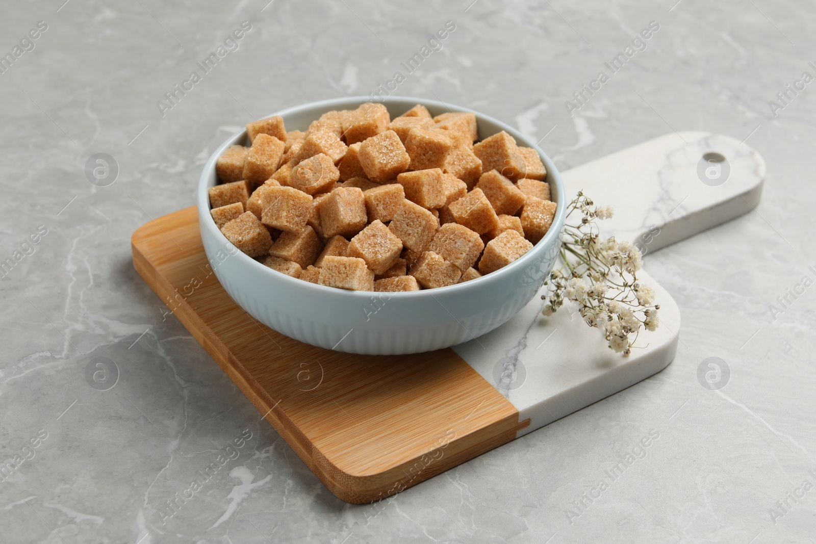 Photo of Bowl of brown sugar cubes on light grey marble table