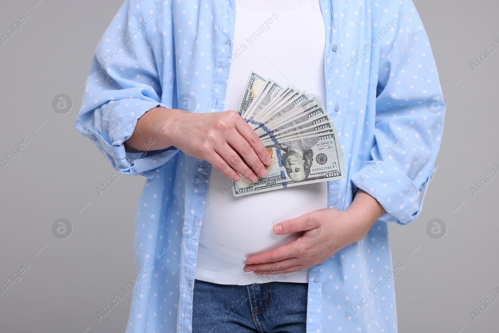 Photo of Surrogate mother. Pregnant woman with dollar banknotes on light grey background, closeup