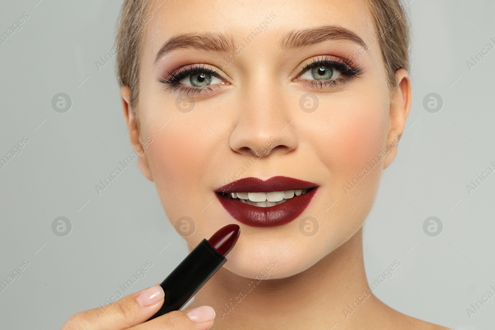 Photo of Beautiful woman applying dark lipstick on gray background