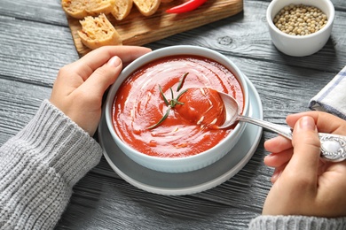 Photo of Woman eating fresh homemade tomato soup at wooden table, closeup