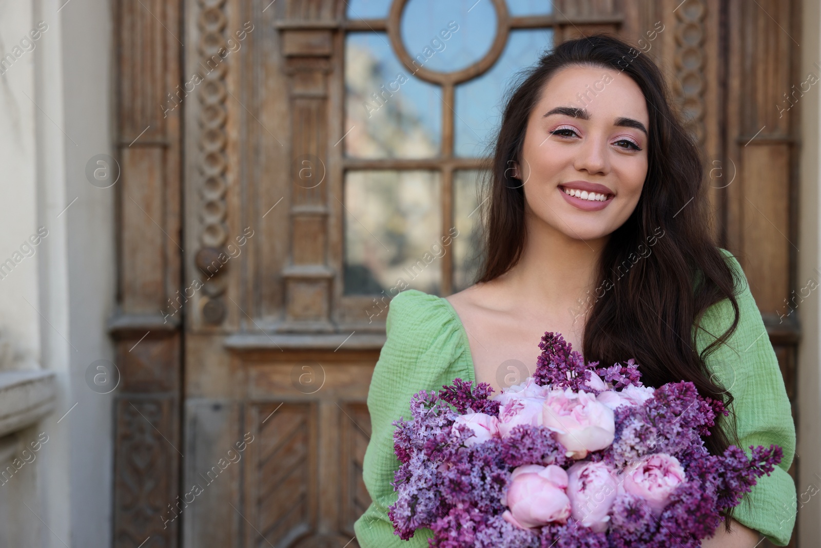 Photo of Beautiful woman with bouquet of spring flowers near building outdoors, space for text