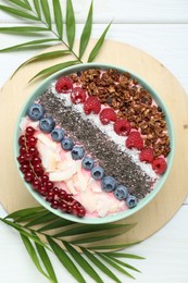 Photo of Tasty smoothie bowl with fresh berries and palm leaves on white wooden table, flat lay
