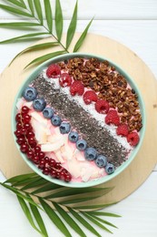 Tasty smoothie bowl with fresh berries and palm leaves on white wooden table, flat lay