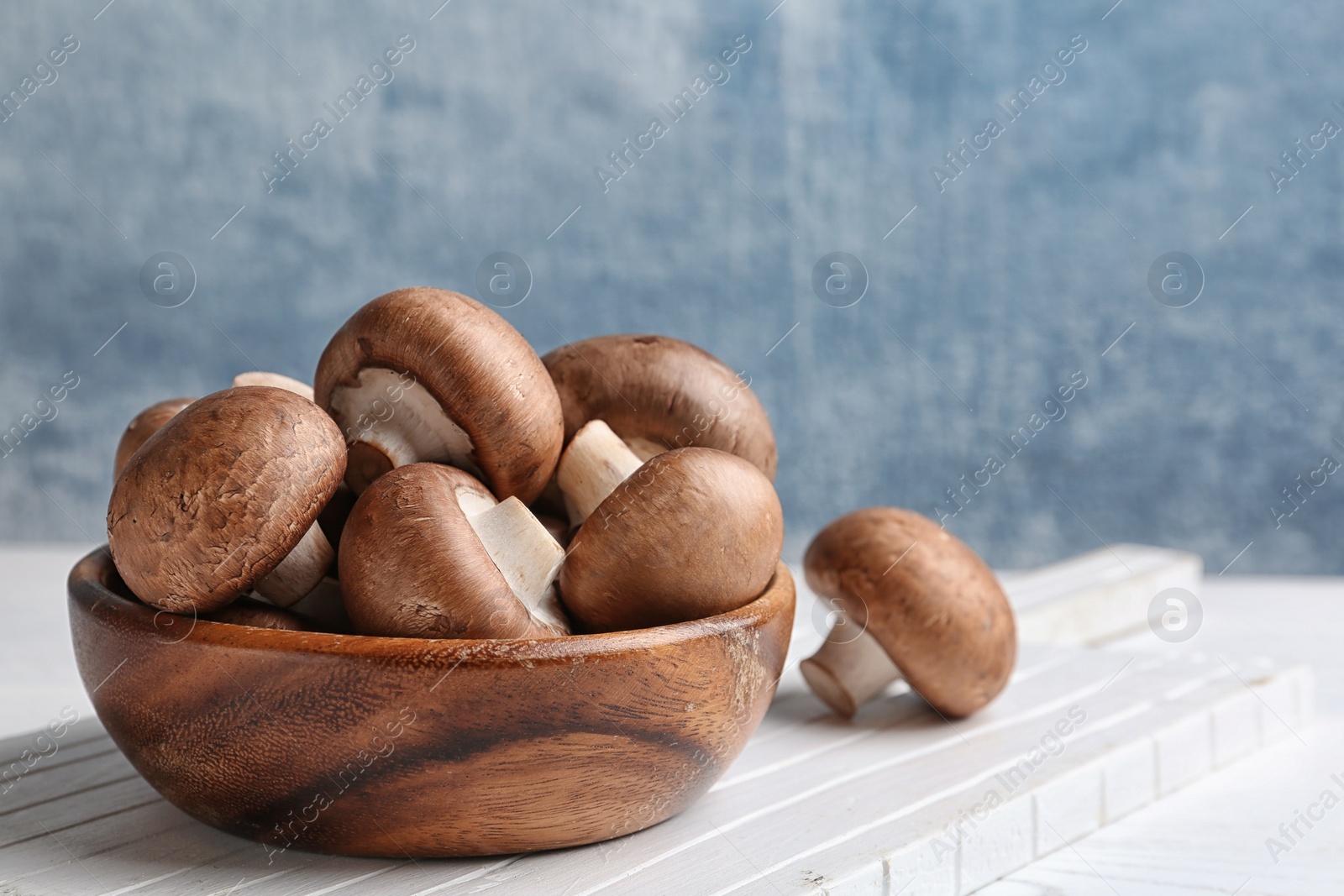 Photo of Bowl with fresh champignon mushrooms on wooden table. Space for text