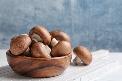 Photo of Bowl with fresh champignon mushrooms on wooden table. Space for text