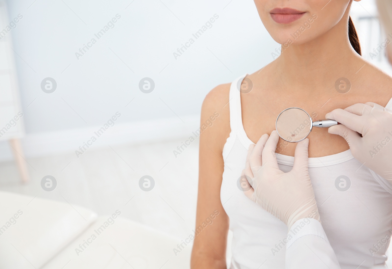 Photo of Dermatologist examining patient's birthmark with magnifying glass in clinic, closeup. Space for text