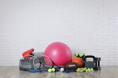 Set of different sports equipment on floor near white brick wall, space for text