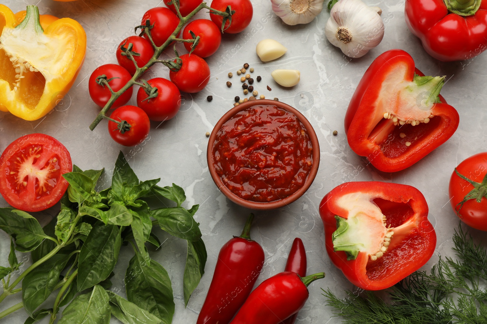 Photo of Delicious adjika sauce in bowl and ingredients on light marble table, flat lay