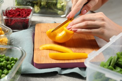 Photo of Woman cutting bell pepper and containers with fresh products on table, closeup. Food storage