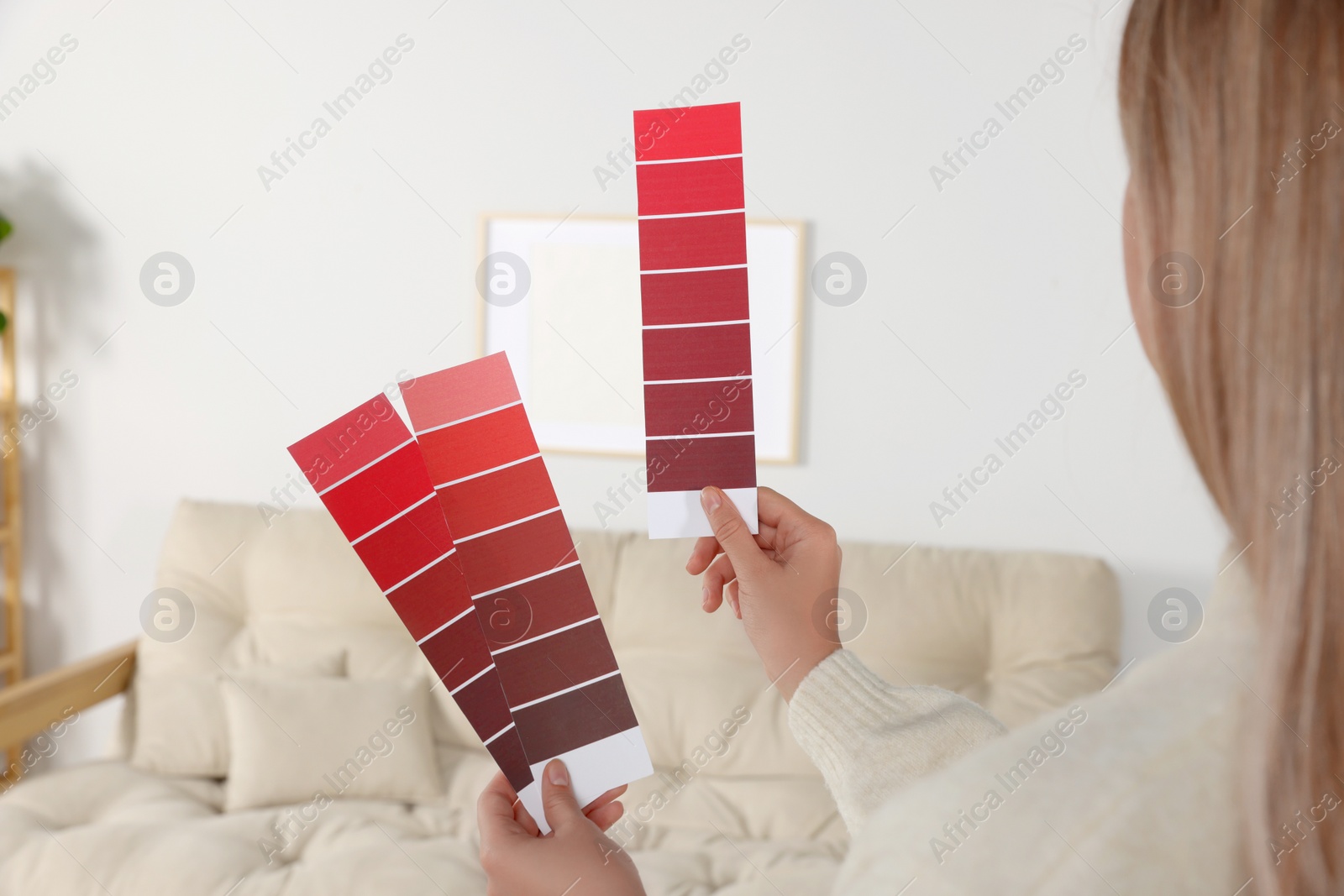 Photo of Woman choosing color for wall in room, focus on hands with paint chips. Interior design
