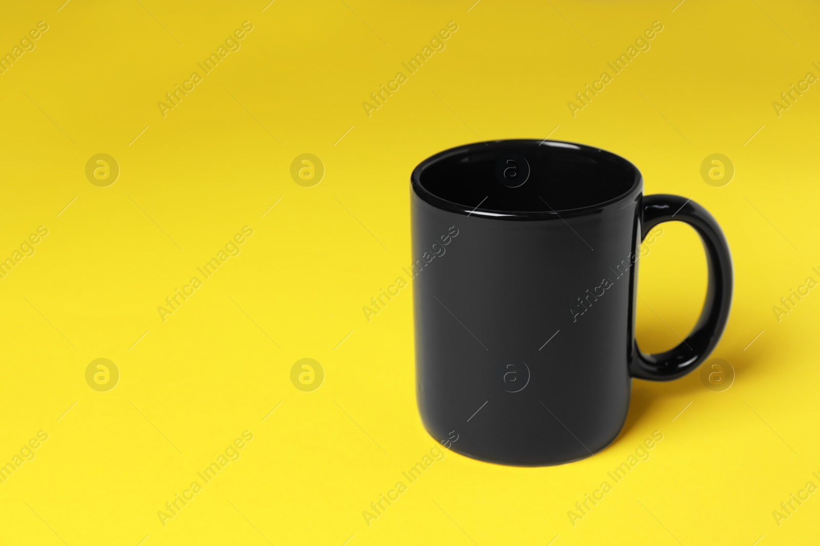 One black ceramic mug on yellow background, space for text Photo of One black ceramic mug on yellow background, space for text