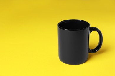 Photo of One black ceramic mug on yellow background, space for text