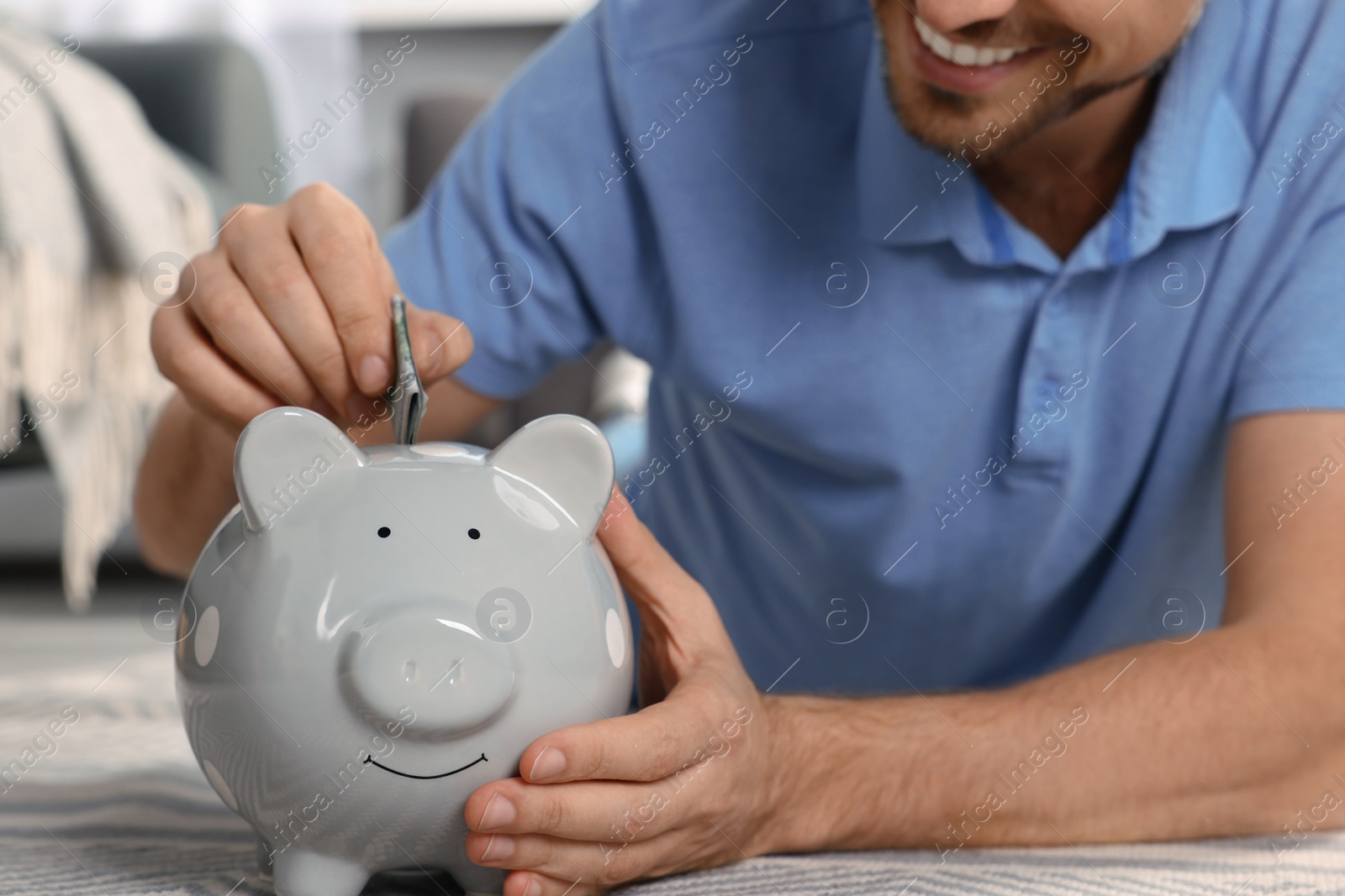 Photo of Happy man putting money into piggy bank at home, closeup