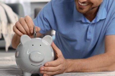 Photo of Happy man putting money into piggy bank at home, closeup