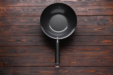 Photo of Empty iron wok on wooden table, top view. Chinese cookware