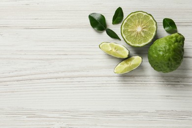Photo of Fresh ripe bergamot fruits with green leaves on white wooden table, flat lay. Space for text
