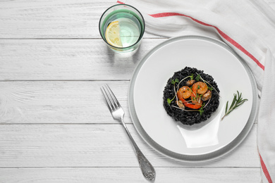 Photo of Delicious black risotto with seafood served on white wooden table, flat lay. Space for text
