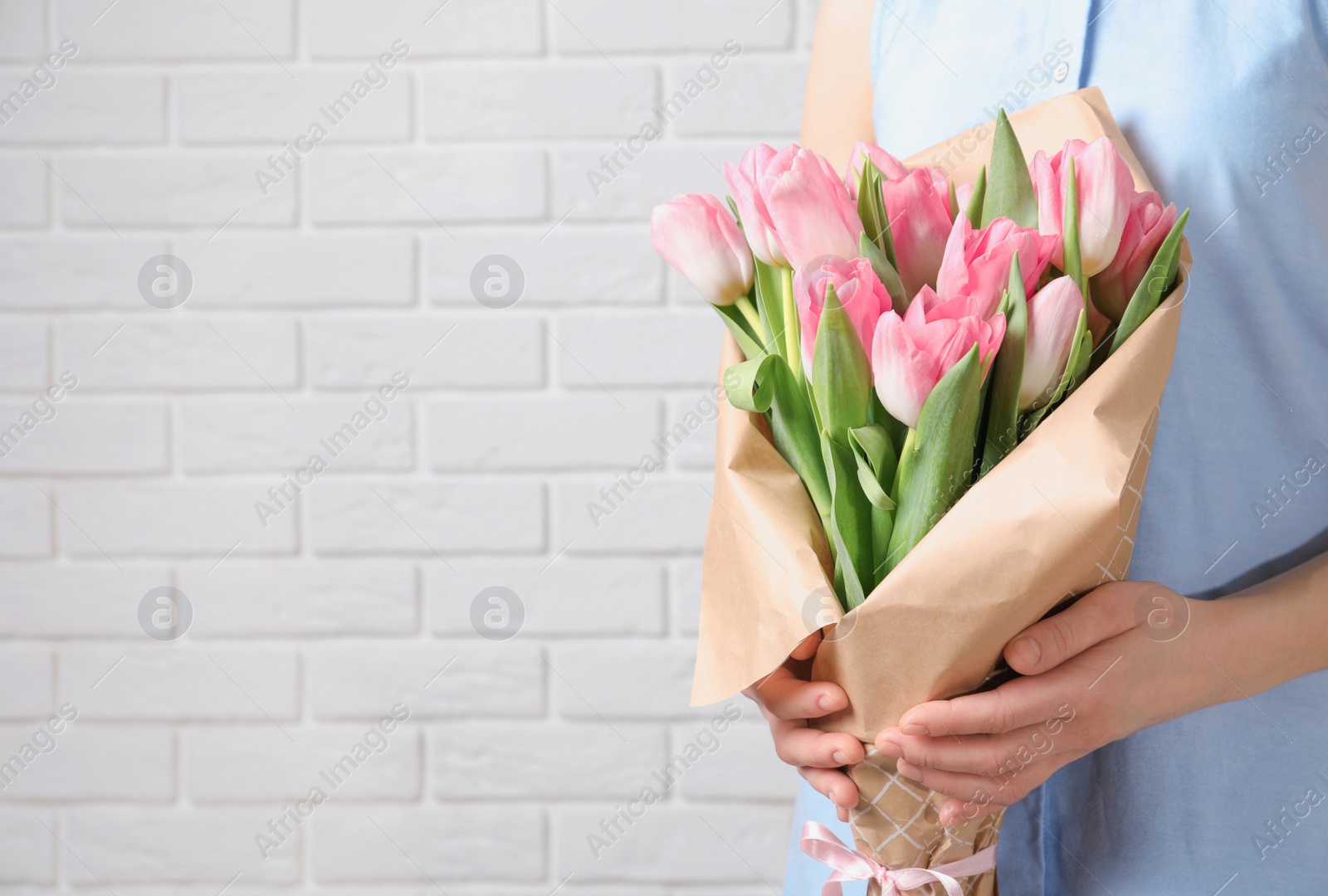 Photo of Girl holding bouquet of beautiful spring tulips near brick wall, closeup with space for text. International Women's Day