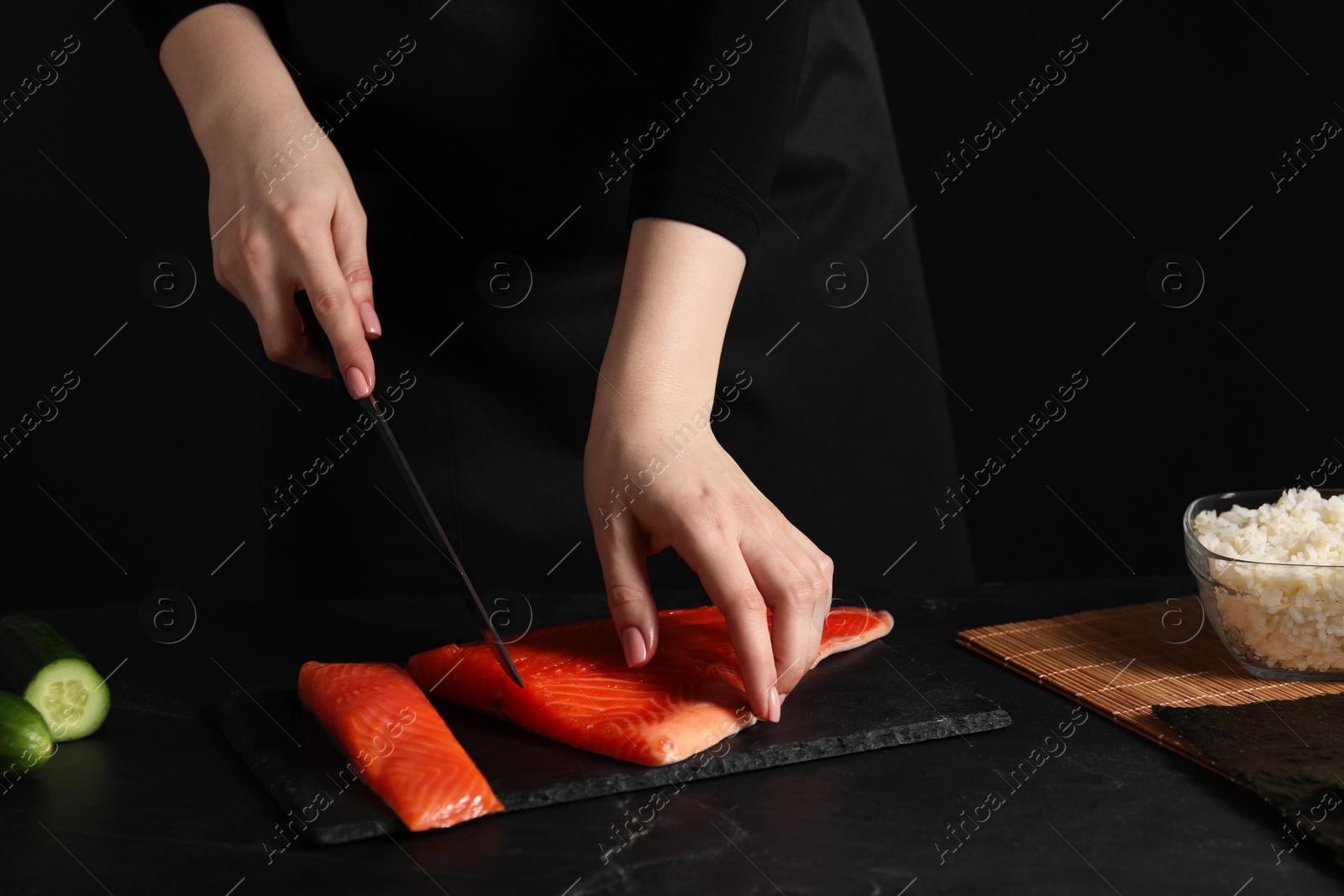 Photo of Chef cutting salmon for sushi at dark textured table, closeup