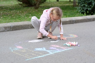 Photo of Little child drawing white clouds with chalk on asphalt