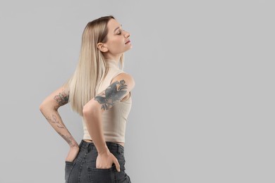 Portrait of beautiful tattooed woman on gray background, space for text