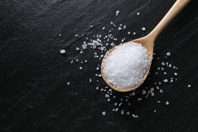 Photo of Organic white salt and spoon on black table, top view. Space for text