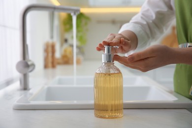 Woman washing hands with liquid soap in kitchen, closeup