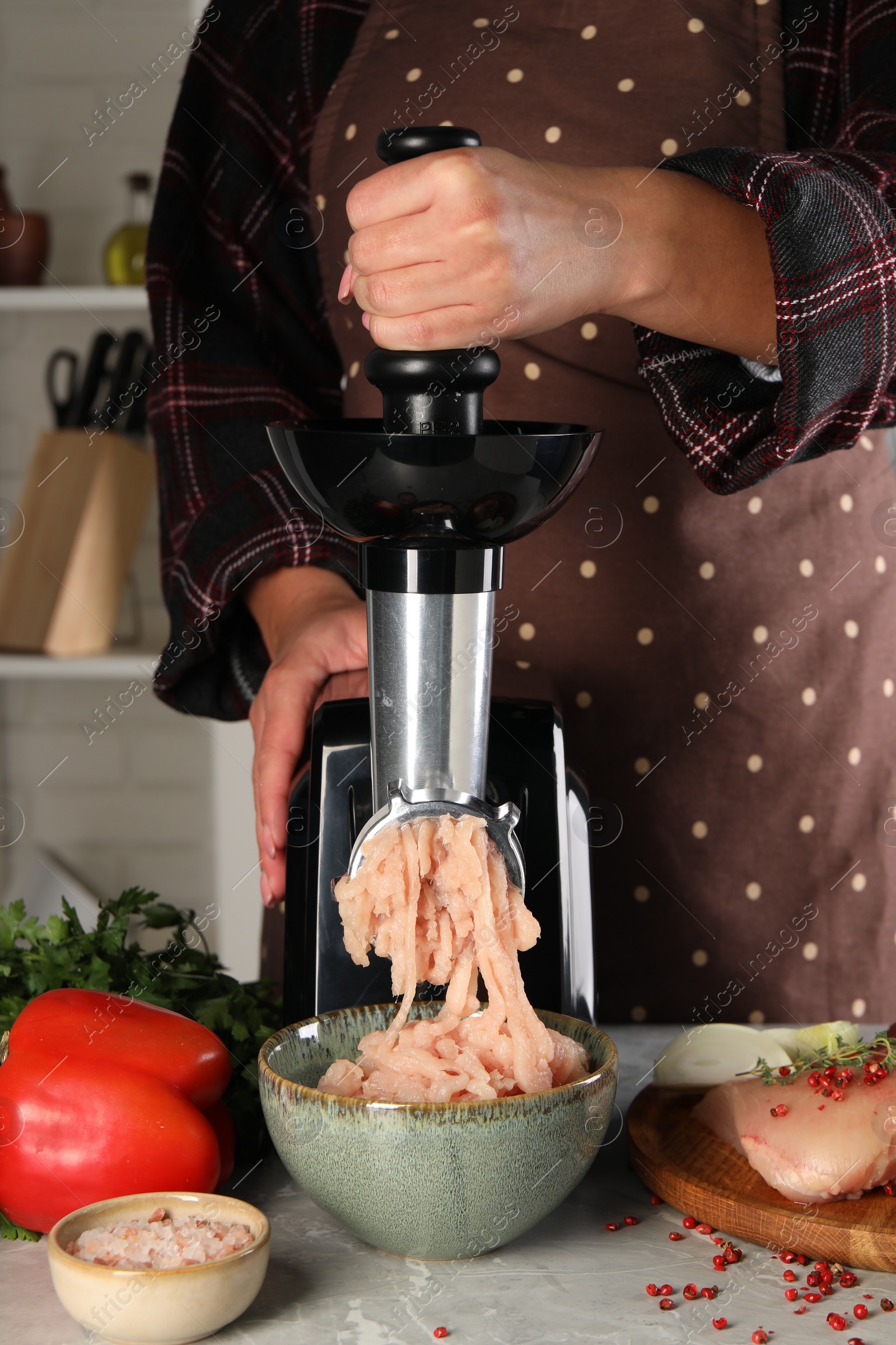 Photo of Woman making chicken mince with electric meat grinder at grey marble table indoors, closeup