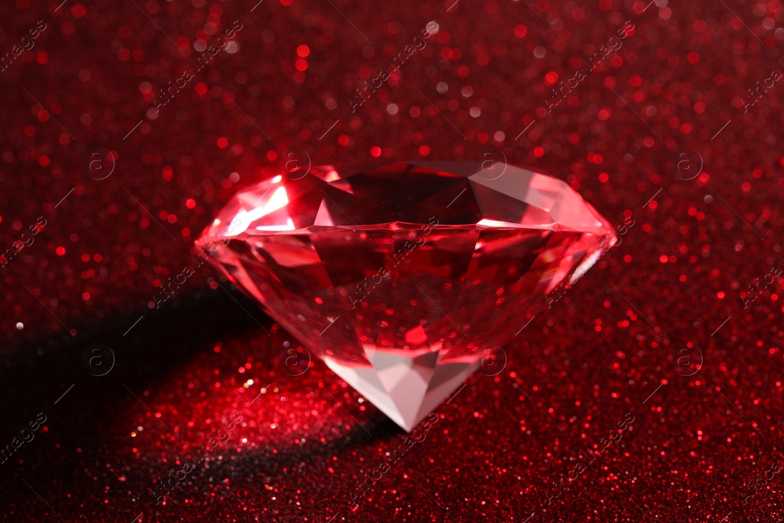 Photo of Beautiful shiny diamond on red glitter background