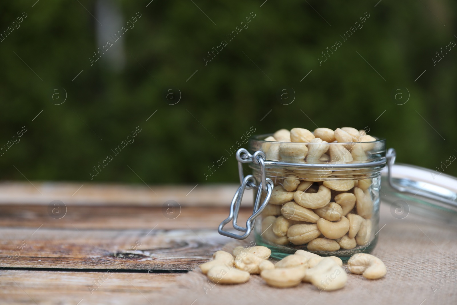 Photo of Tasty cashew nuts in glass jar on wooden table outdoors, space for text