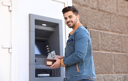 Photo of Young man with money near cash machine outdoors