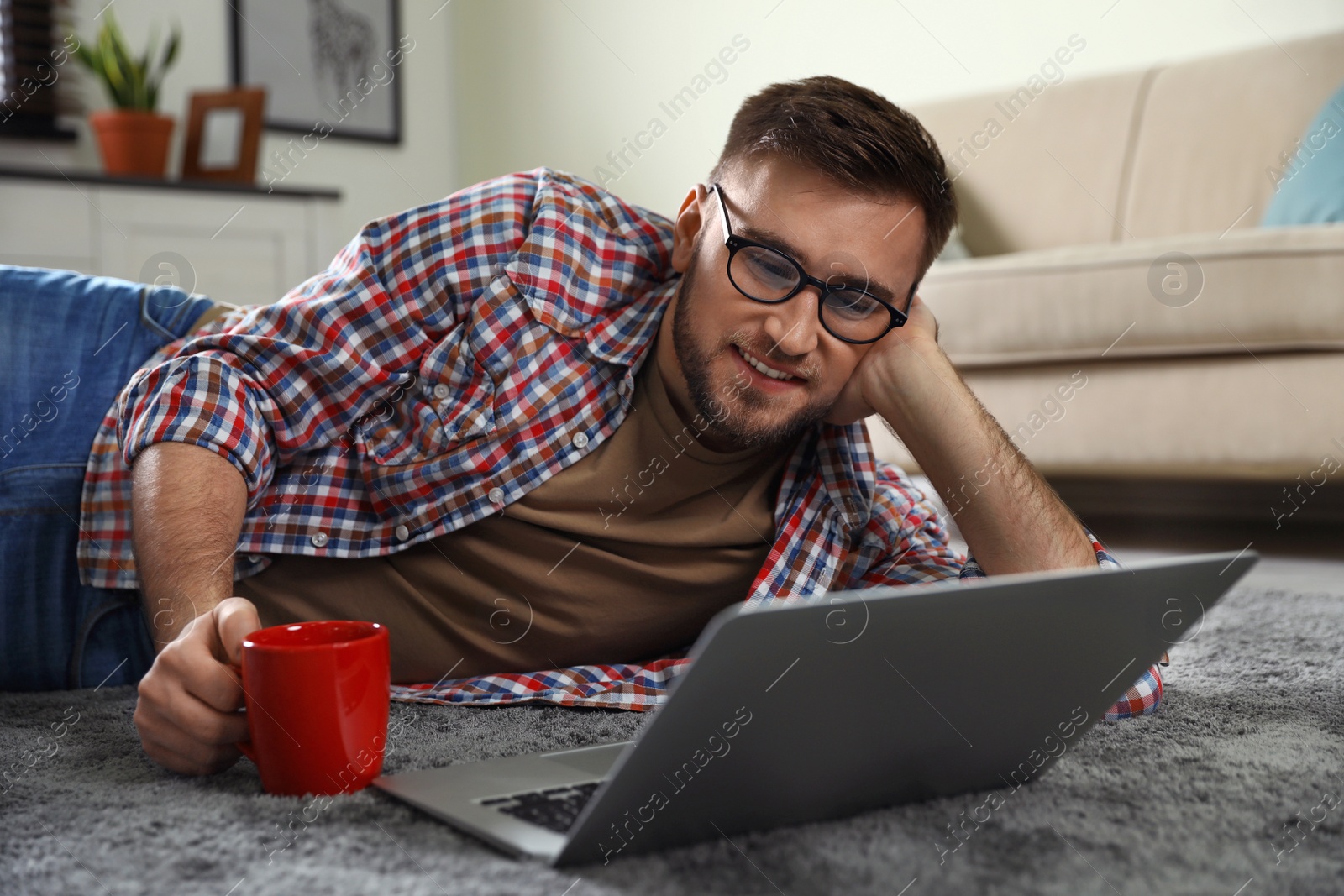 Photo of Young man using laptop while lying on floor in living room