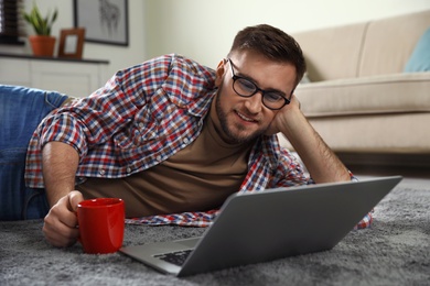Young man using laptop while lying on floor in living room