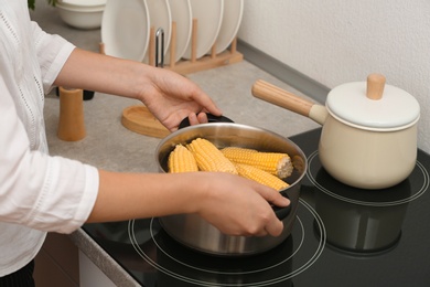 Photo of Woman preparing corn in stewpot on stove, closeup