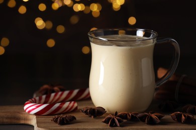 Photo of Glass of delicious eggnog with anise stars and candy cane on wooden table