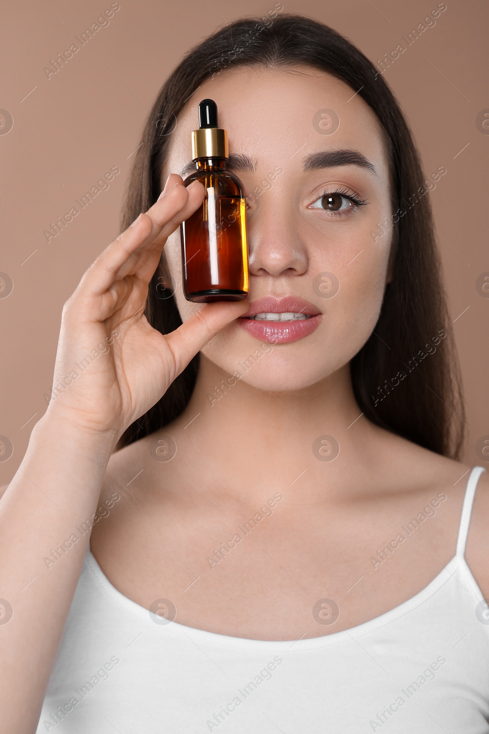 Photo of Beautiful young woman with bottle of essential oil on brown background