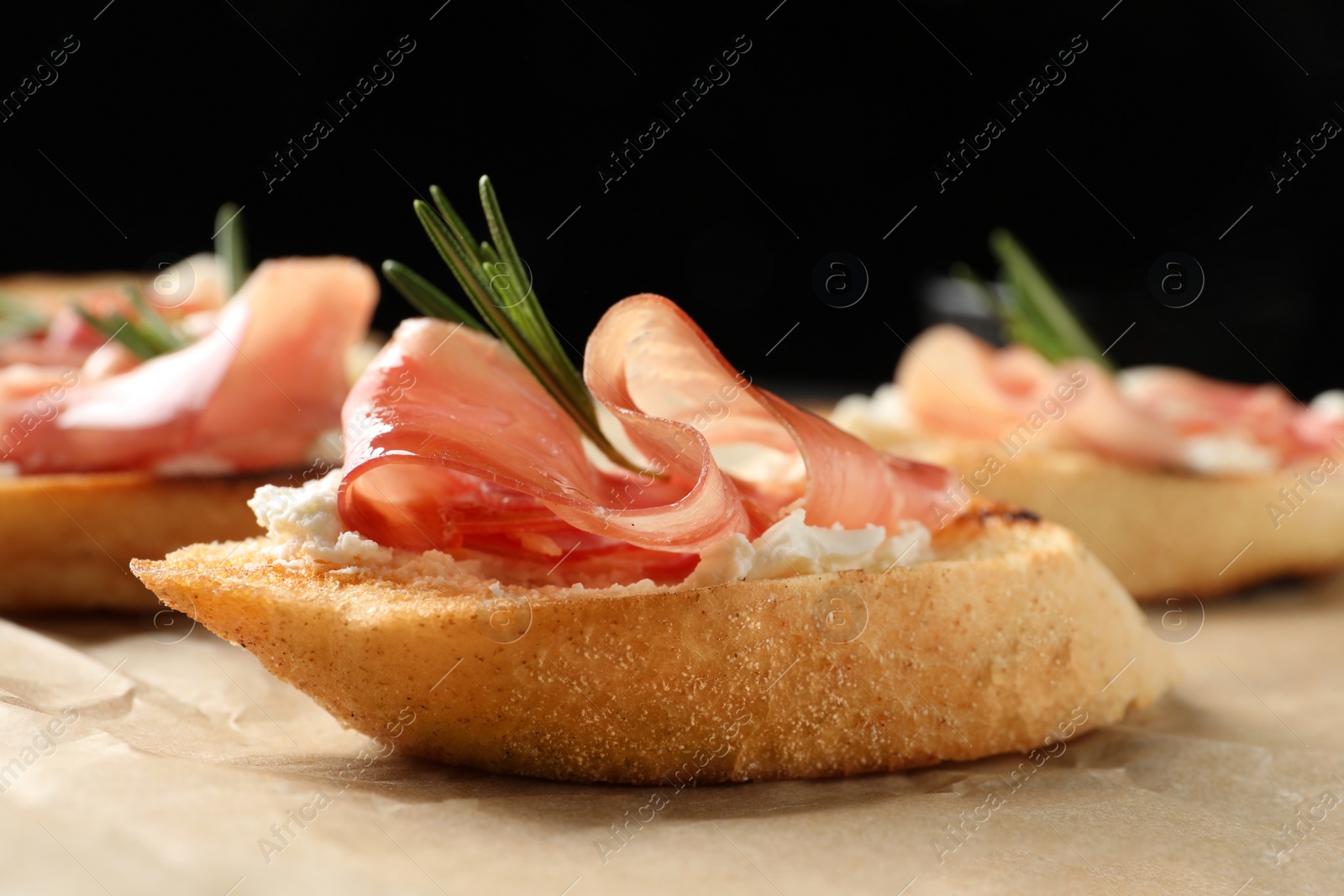 Photo of Tasty bruschettas with prosciutto and cream cheese served on table against dark background, closeup. Space for text