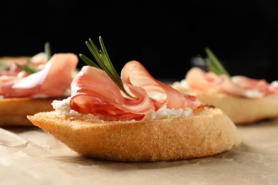 Photo of Tasty bruschettas with prosciutto and cream cheese served on table against dark background, closeup. Space for text