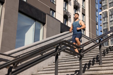 Happy man running down stairs outdoors on sunny day, low angle view. Space for text