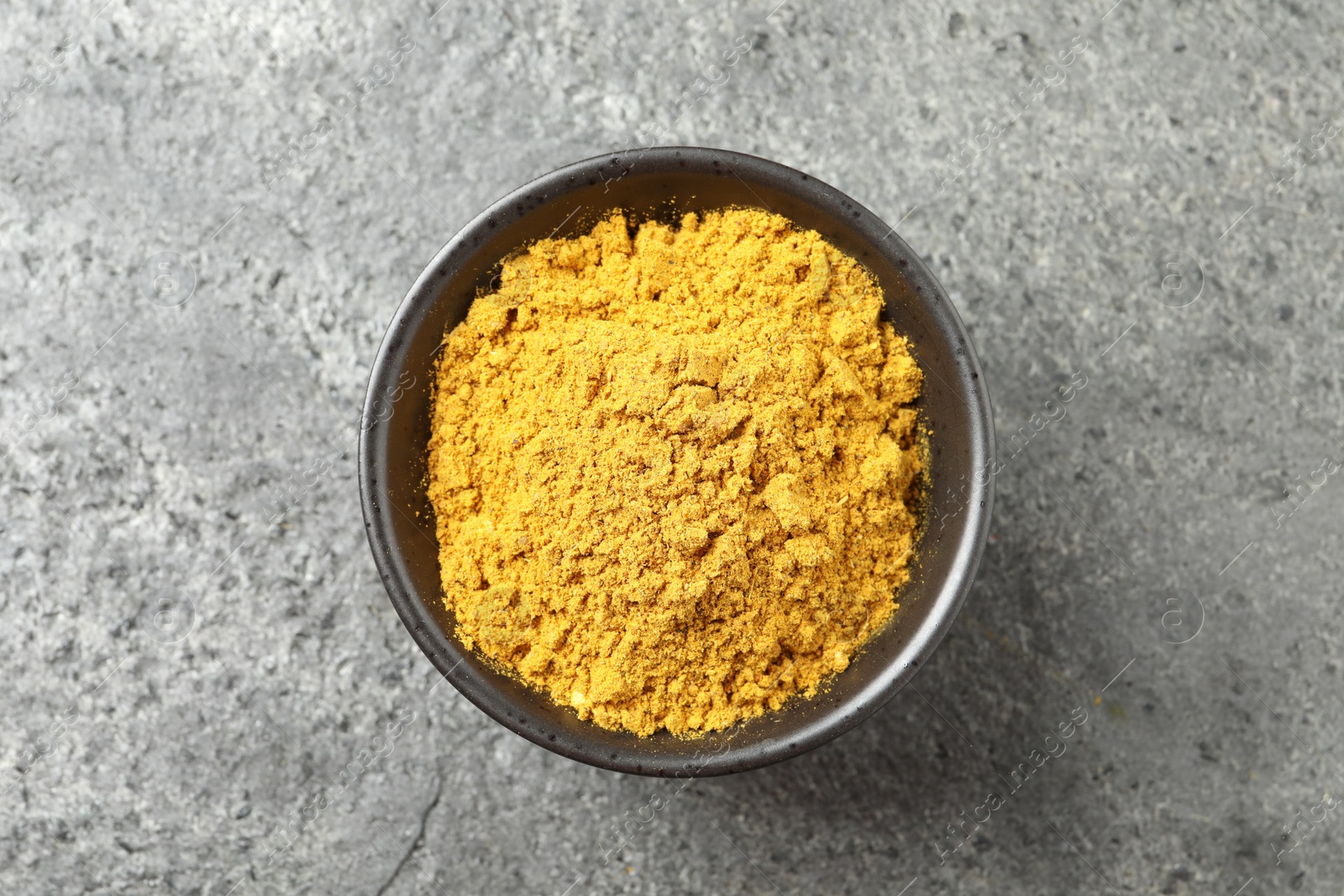 Photo of Dry curry powder in bowl on dark textured table, top view