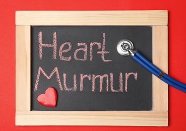 Blackboard with text HEART MURMUR and stethoscope on color background, top view