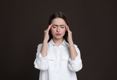 Photo of Young woman suffering from headache on brown background